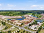 Aerial view of a housing development under construction with winding roads, multiple ponds, and surrounding green fields.