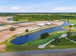 Aerial view of a newly developing area beside a finished golf course with winding water hazards and dirt lots awaiting buildings.