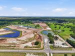 Aerial view of a developing housing subdivision with winding roads, dirt lots, and small ponds amid green fields.