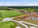 Aerial view of a golf course under construction with green fairways, sand traps, and nearby construction site buildings and equipment