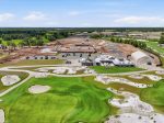 Aerial view of a golf course under construction, with greens, sand bunkers, a clubhouse, and construction zones in the background