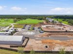Aerial view of a construction site next to a lush golf course, with heavy machinery, dirt roads, and a large white temporary building surrounded by a parking area of cars and vans in the foreground.