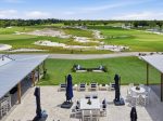 Patio dining area overlooking a lush golf course with sand bunkers and a blue-sky backdrop.