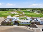Aerial view of a lush golf course with fairways, sand bunkers, and water features, seen from above the clubhouse area.
