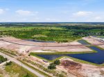 Aerial view of a large construction site with curved road, pink soil, and several water-filled ponds surrounded by green fields.
