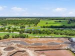 Aerial view of a construction site at the edge of a lush golf course with ponds and winding paths under a blue sky.