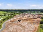 Aerial view of a construction site next to a golf course, with dirt, machinery, and a white tent building.