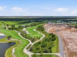 Aerial view of a lush golf course with greens, fairways, water hazards, and a construction site on the right under a blue sky.