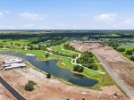 Aerial view of a winding golf course with green fairways, water hazards, and a nearby construction site and roads under development