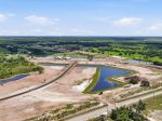 Aerial view of a construction site with winding roads, ponds, and cleared dirt lots amid green fields.