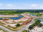 Aerial view of a construction site with winding roads, dirt lots, and several man-made ponds surrounded by green fields and trees.