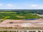 Aerial view of a construction site with curved road, roundabout, bare dirt lots, and ponds surrounded by green fields.