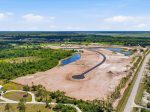 Aerial view of a suburban construction site with a winding asphalt road, ponds, and surrounding trees and fields.