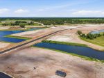 Aerial view of a construction site with a paved road cutting through dusty ground and several blue retention ponds nearby.