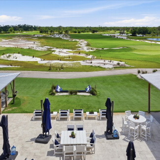 Patio dining area overlooking a lush golf course with green fairways and sand bunkers in the distance.